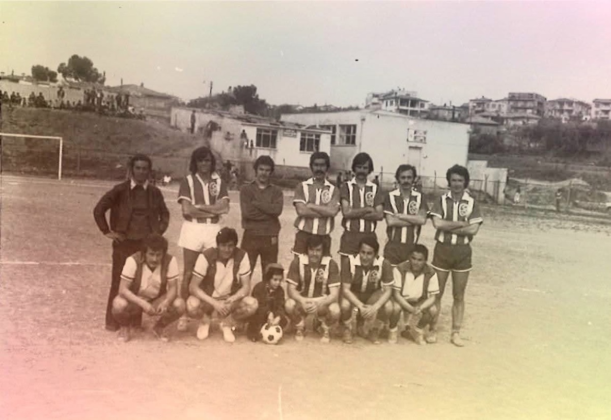 Toprak sahada dizilmiş çizgili formalı futbol takımı